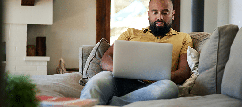 man on couch with laptop searching the best sites for used cars